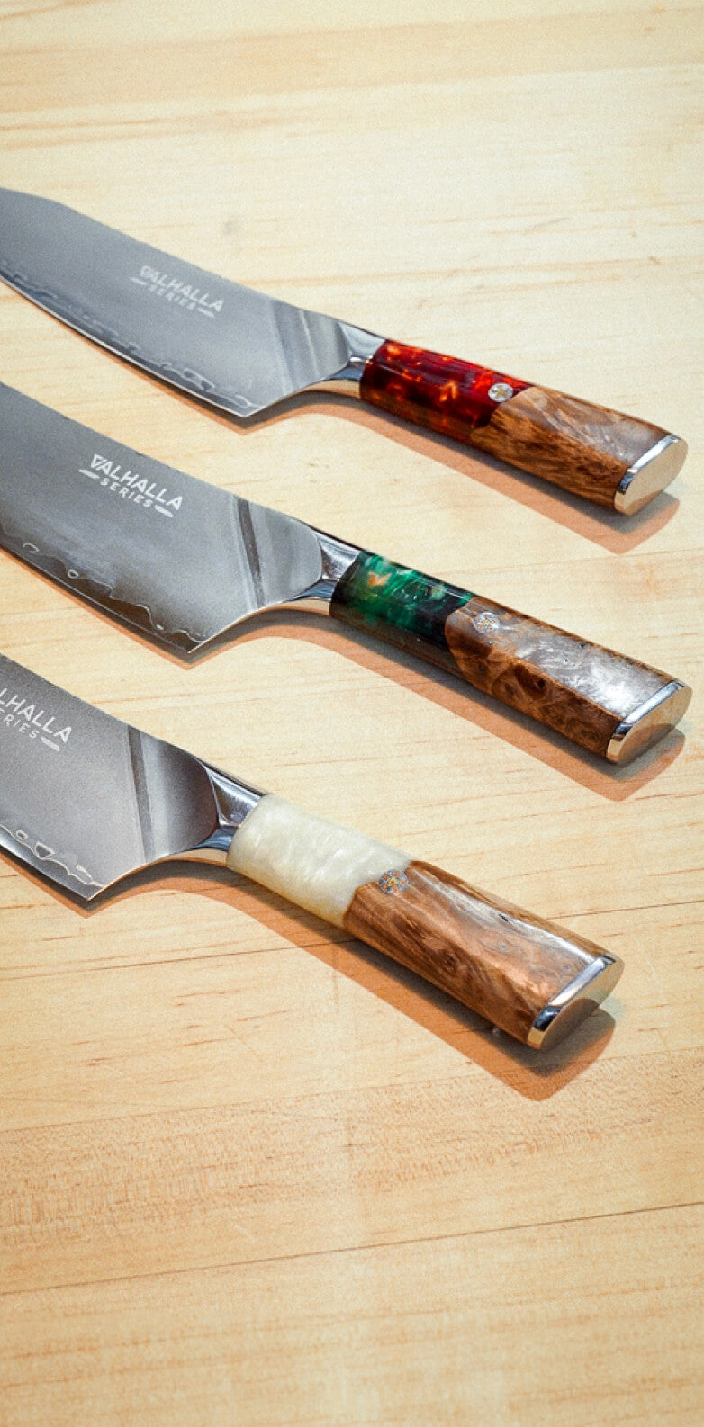 Three Valhalla knives with resin handles laid on a warm beige backdrop