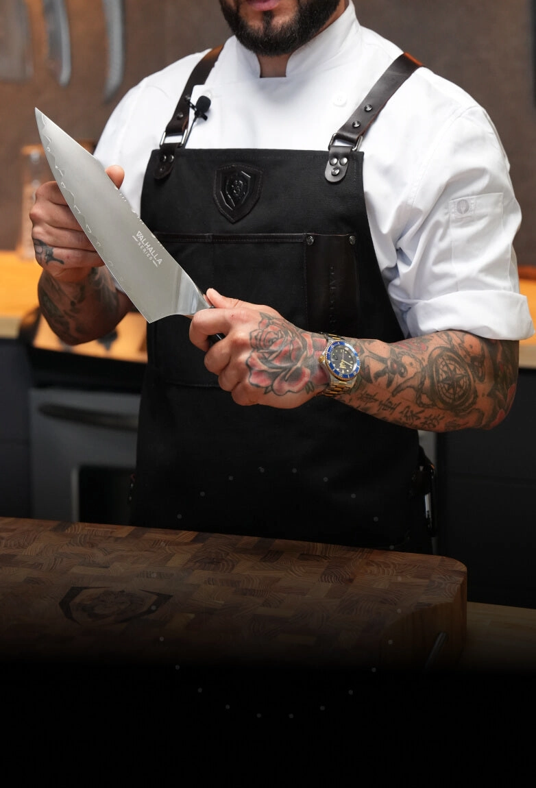 Chef in a black apron holding a Valhalla cleaver in a professional kitchen