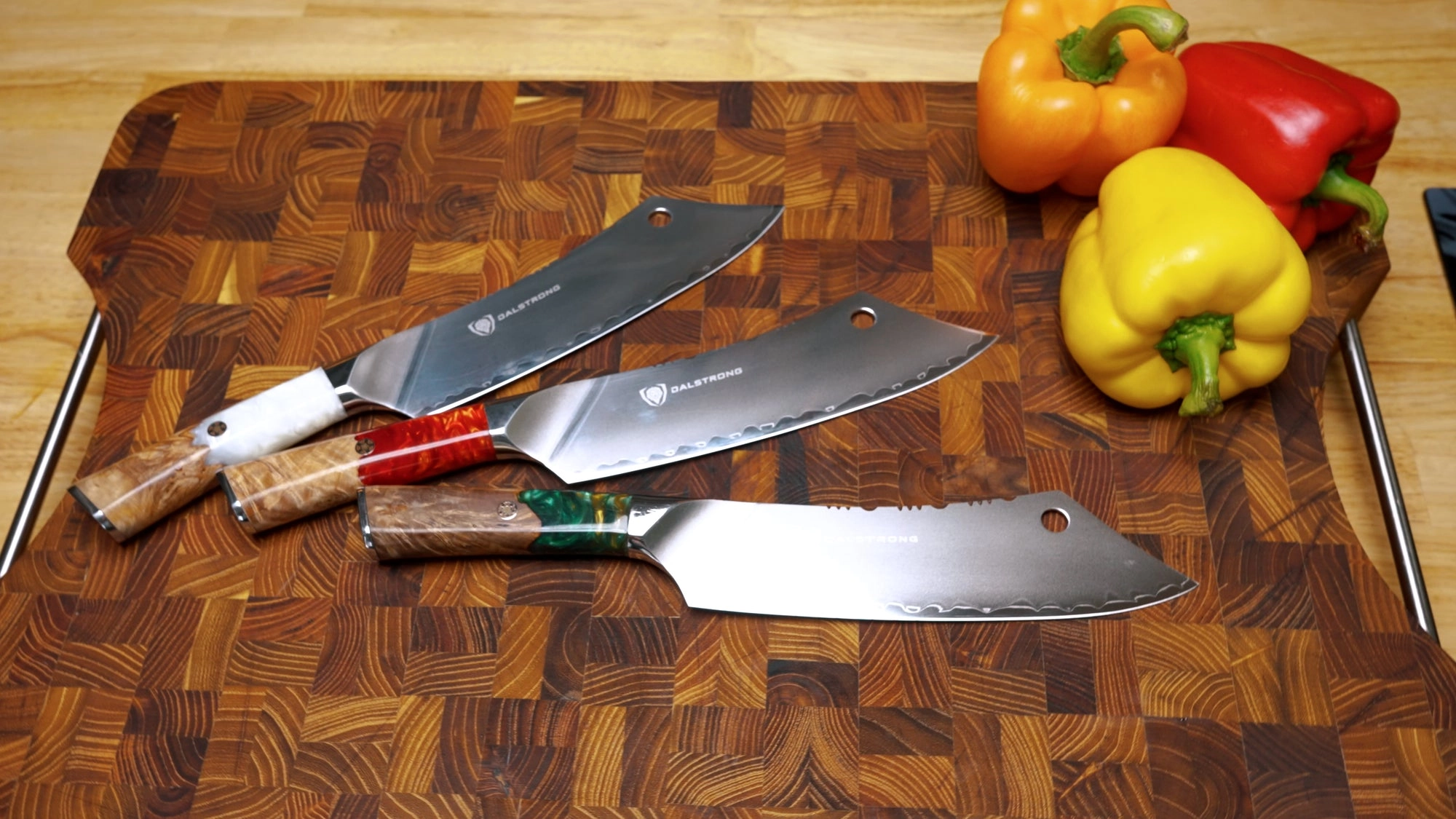 Three Dalstrong Crixus chef and cleaver hybrid knives on a wooden cutting board beside red and yellow peppers