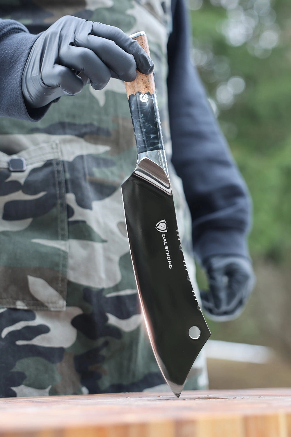 Black-handled hybrid knife standing on a board beside a leather sheath